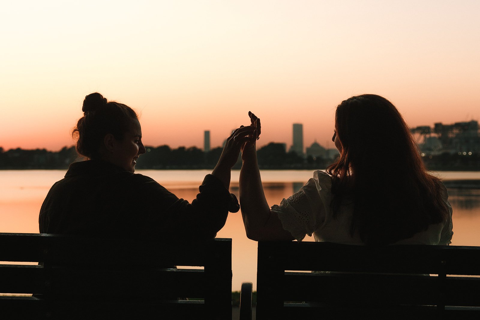 couple holding hands while sitting on a bench looking at the boston sunset.