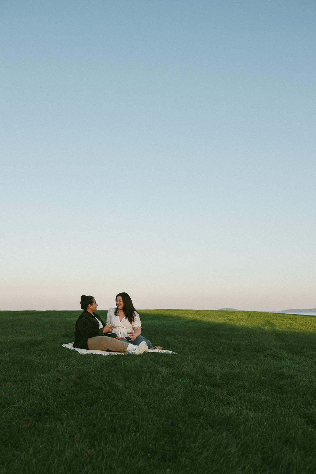 Stunning couple sit on a blanket and share a laugh during their Castle island engagement photoshoot 