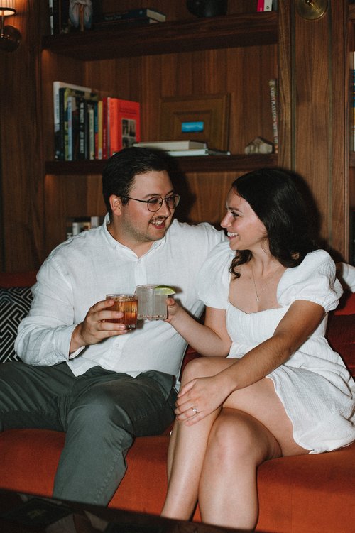 Beautiful couple sit on a couch together sipping cocktails