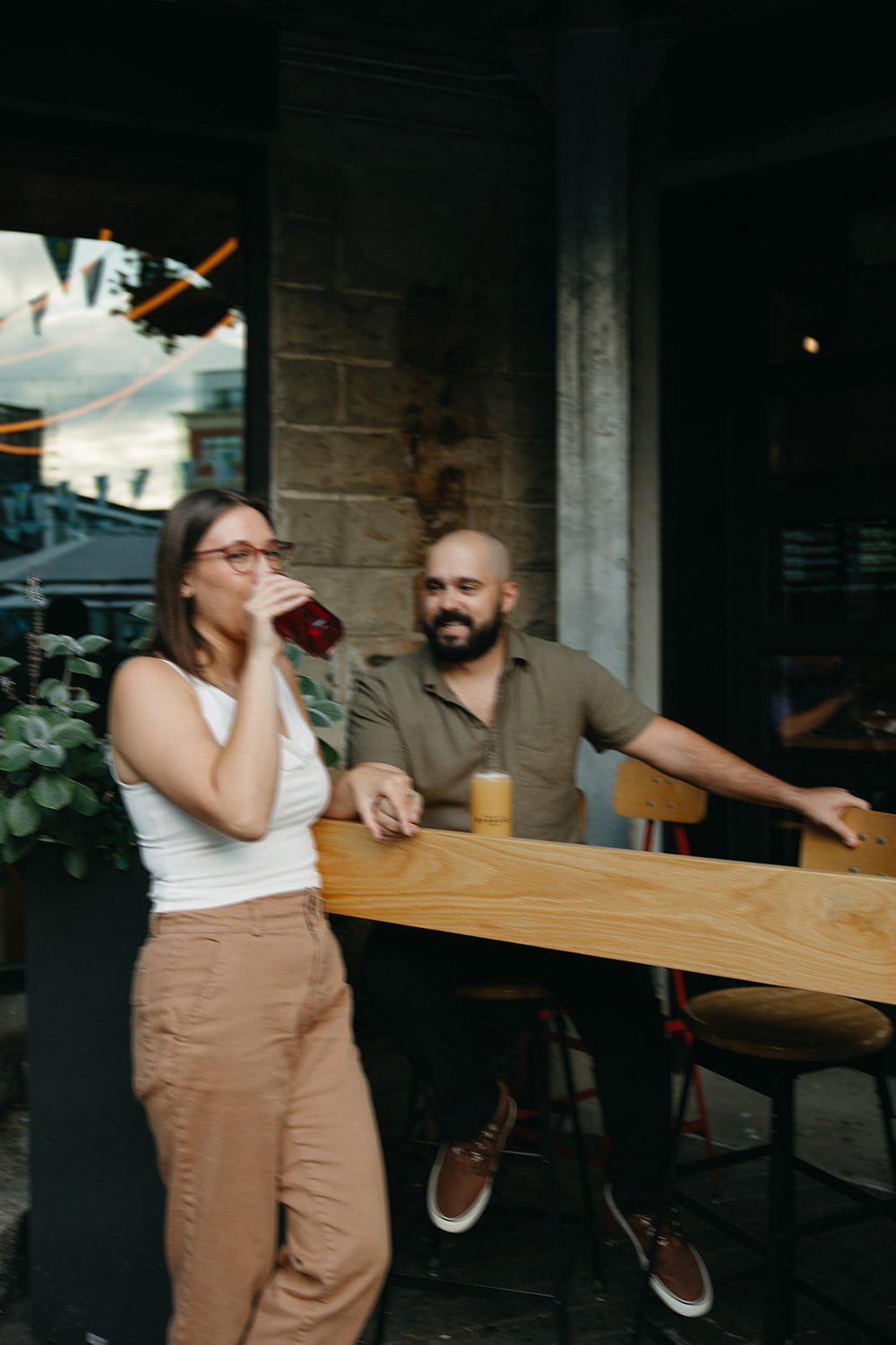 Beautiful couple sit at the bar sharing beers during their Boston engagement photoshoot