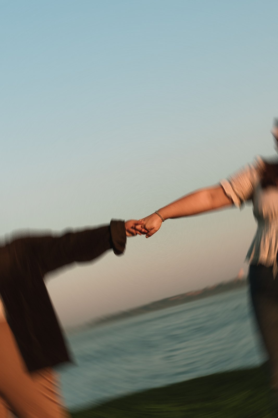 A couple hold hands during their Castle Island Engagement photos with the sea in the backdrop