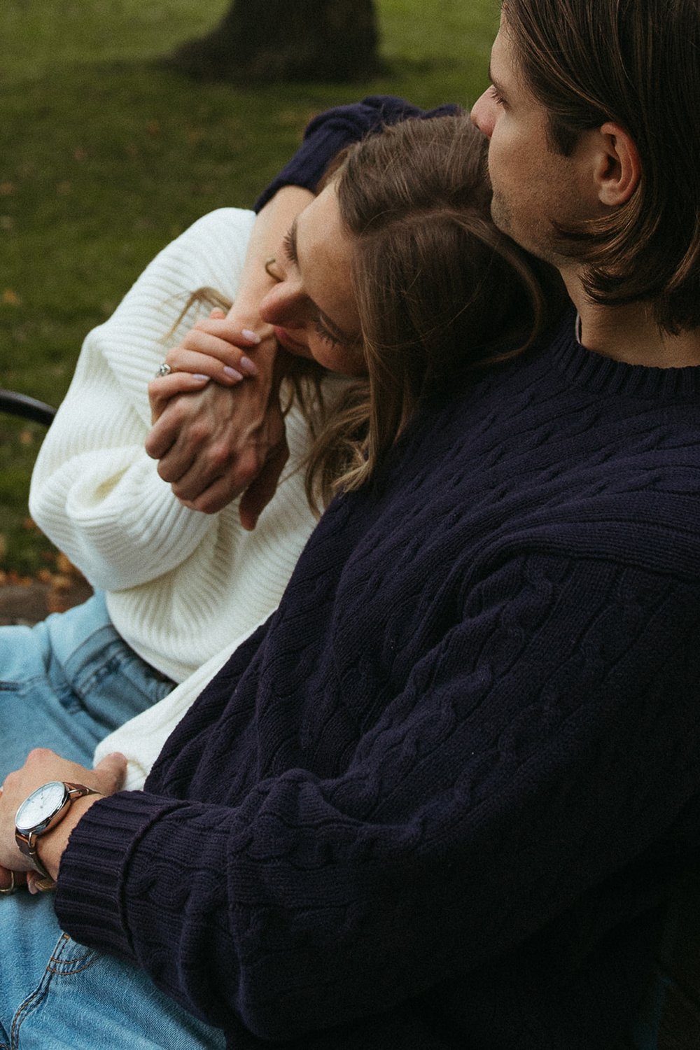 Beautiful couple shaStuning couple sit together on a park bench during their Boston engagement photoshoot