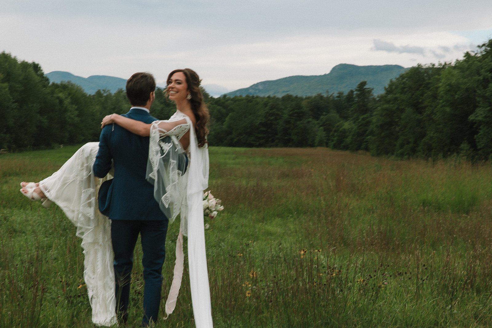 Groom carries his stunning new bride with the mountains in the background