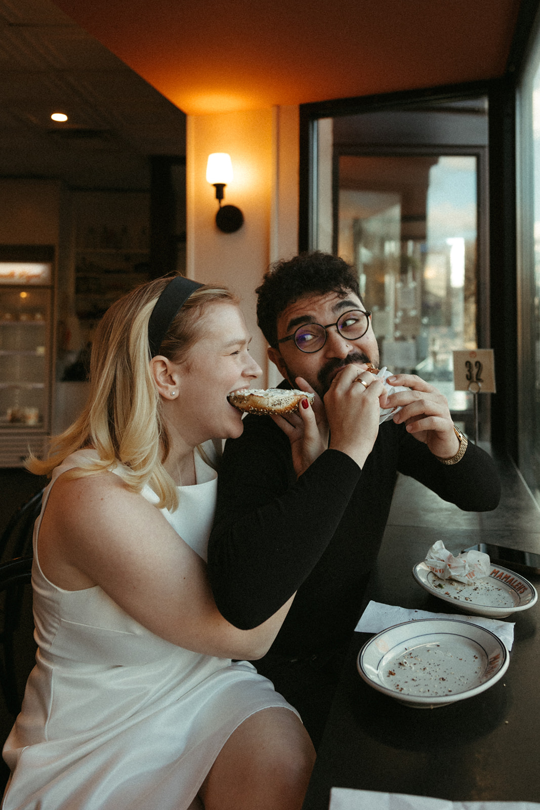 Beautiful couple pose in the cafe eating bagels together