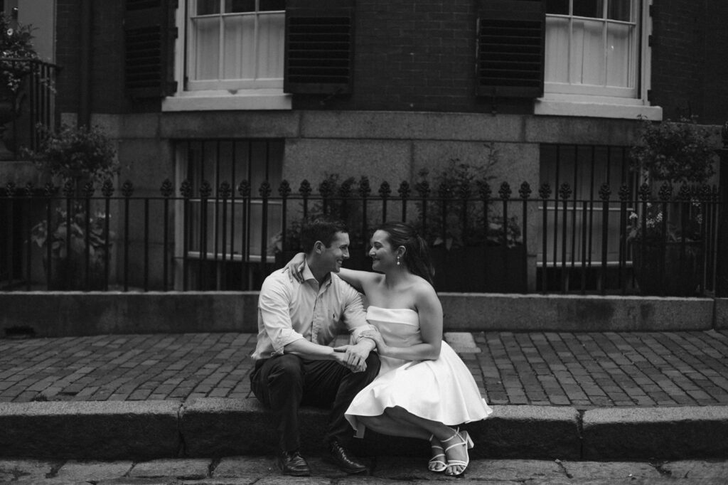 couple sits on curb in beacon hill during engagement photos