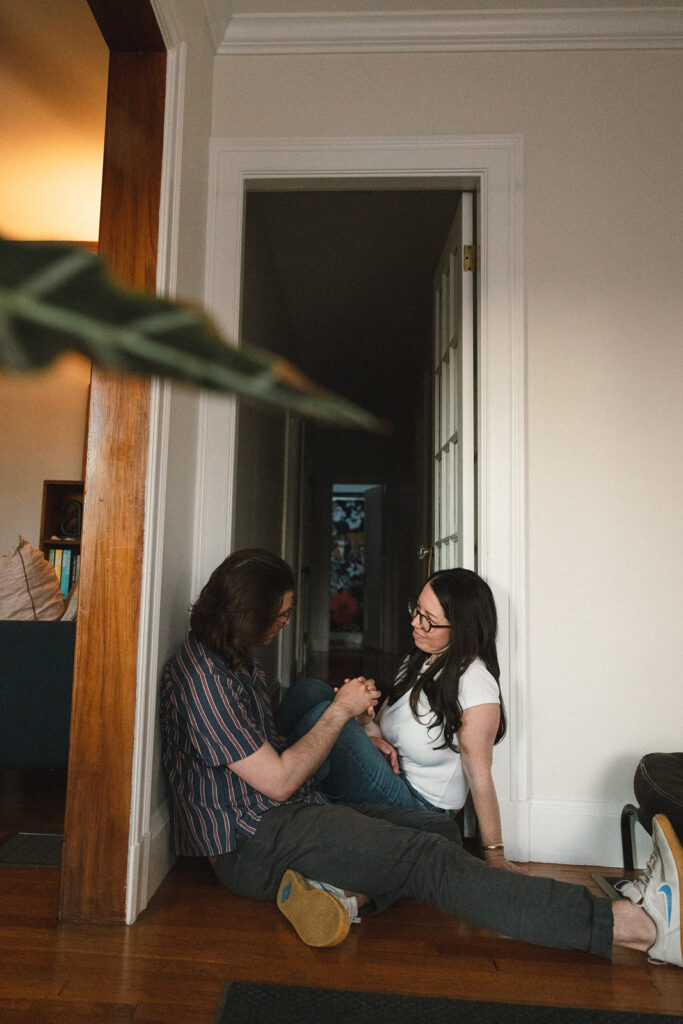 couple sits in doorway and holds hands in their apartment