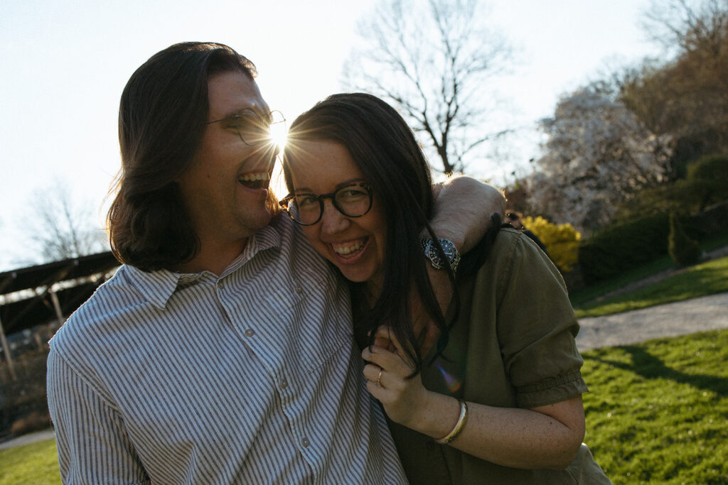 Couple laughs as they walk through Arnold Arboretum during engagement session in spring