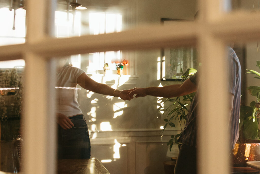 couple dancing around kitchen during sunny film engagement session at their apartment