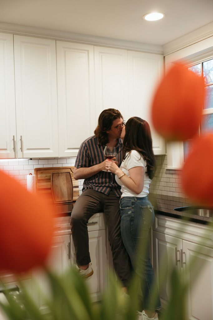 creative photo shot through a vase of tulips of couple drinking wine in their kitchen