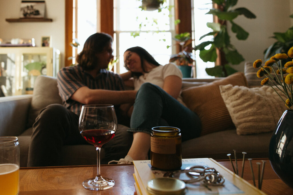 couple sits on couch in cozy apartment during at home engagement session in boston