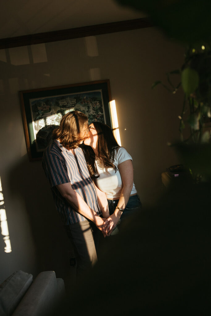 Couple kisses during at-home, film-inspired engagement session in their apartment during golden hour