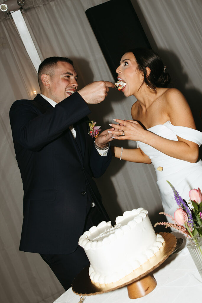 groom feeds bride a big bite of cake during funny cake cutting photos