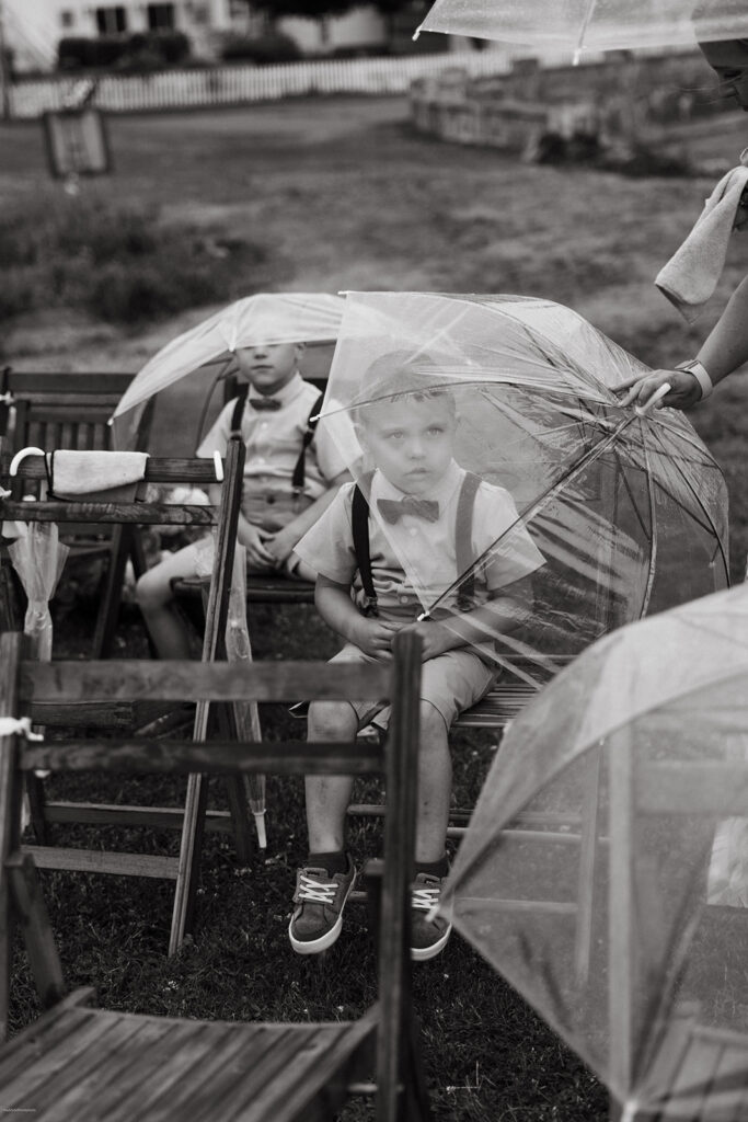 little boy sits under umbrella during rainy massachusetts wedding ceremony