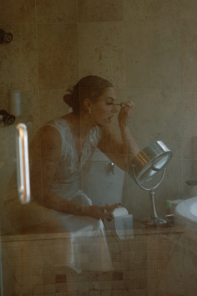 creative photo of bride getting ready in bathroom shot through the shower door reflection
