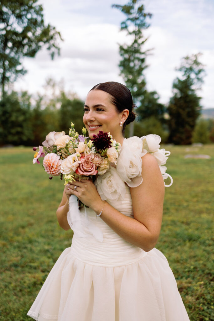 bride with slick back bun holds colorful wedding bouquet and laughs during wedding photos
