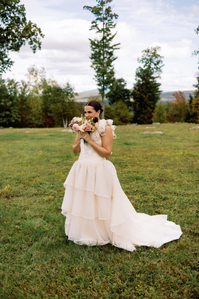 bride poses in vintage wedding gown in field with colorful wedding bouquet with foliage in the background