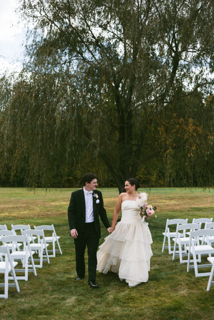 bride and groom walk with willow tree behind them during wedding portraits
