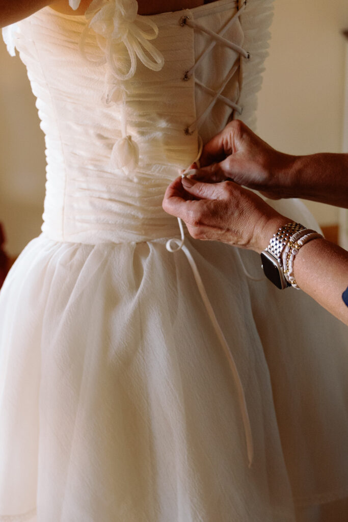 mom helps bride lace her corset on her vintage wedding dress