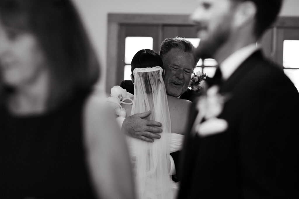 bride and father of the groom share an emotional embrace after backyard wedding ceremony
