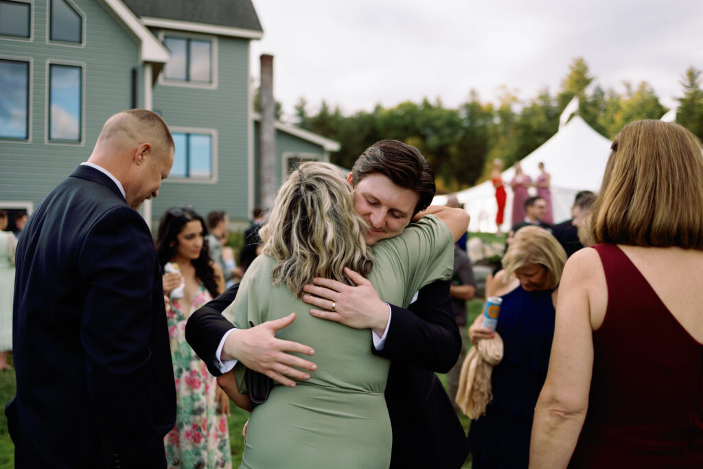 groom embraces friends at cocktail hour during sunset