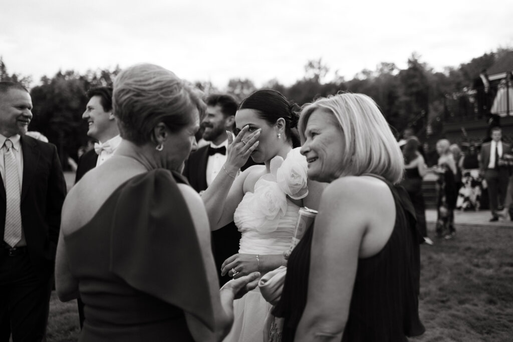 bride wipes a tear during emotional embraces during cocktail hour