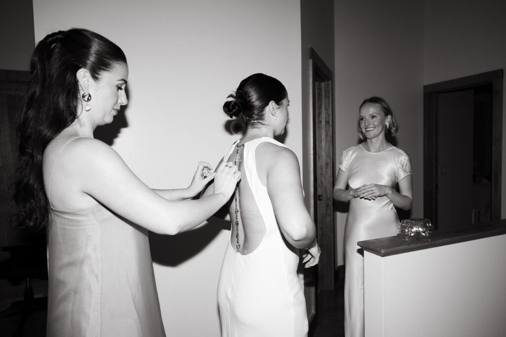 friends help bride put on wedding reception dress