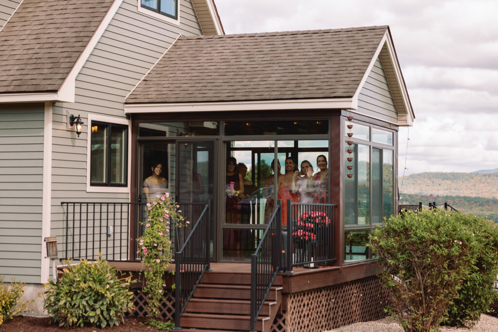 documentary wedding photo of the bride and grooms family watching their first look through the windows of their home at backyard wedding in new hampshire