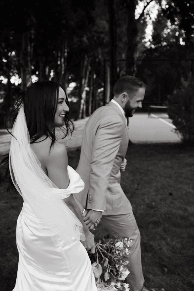 A groom holds his bride's hand as they walk to their coastal wedding ceremony.