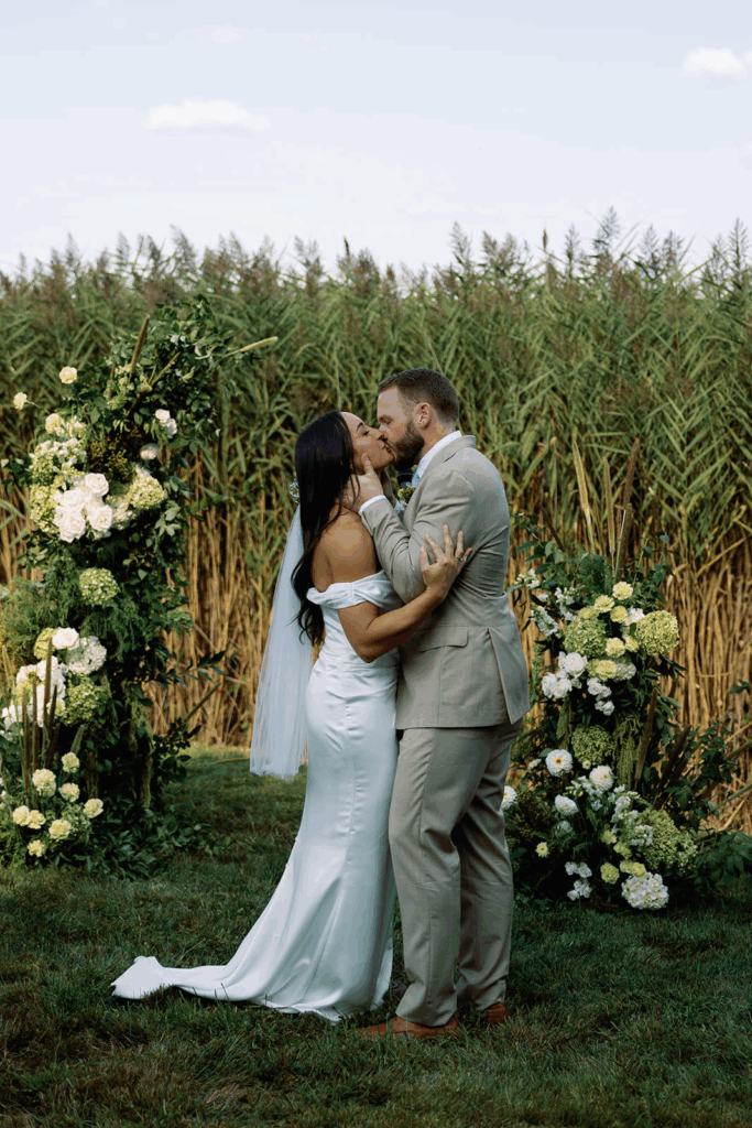 A groom and bride kiss in front of hydrangea decorations after their ceremony.