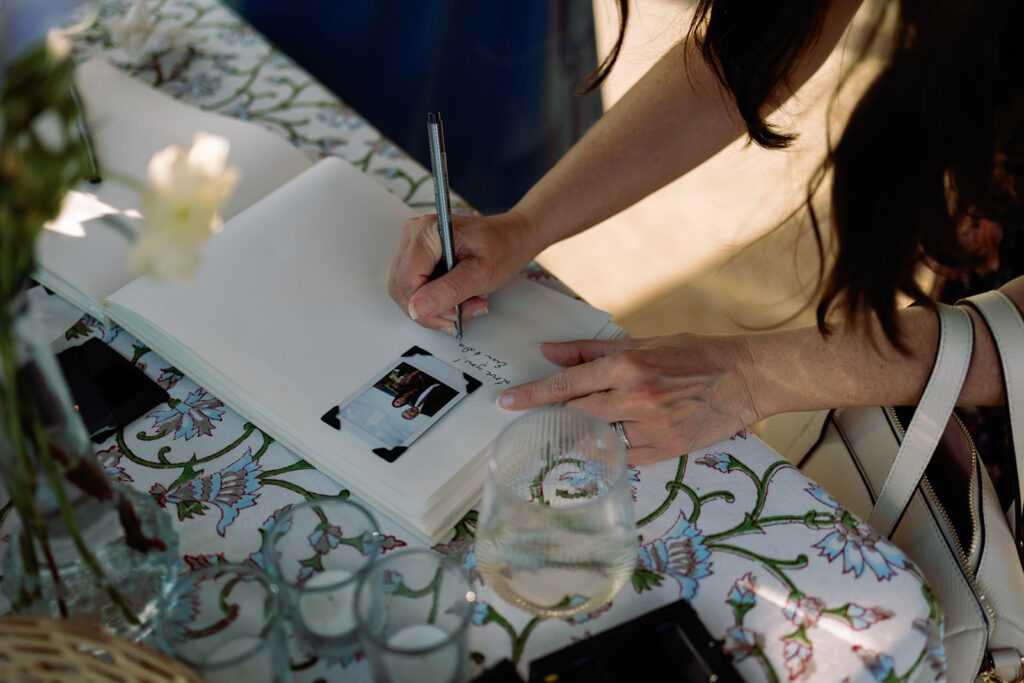 Wedding guest writing a note to the bride and groom underneath a photo in a book.