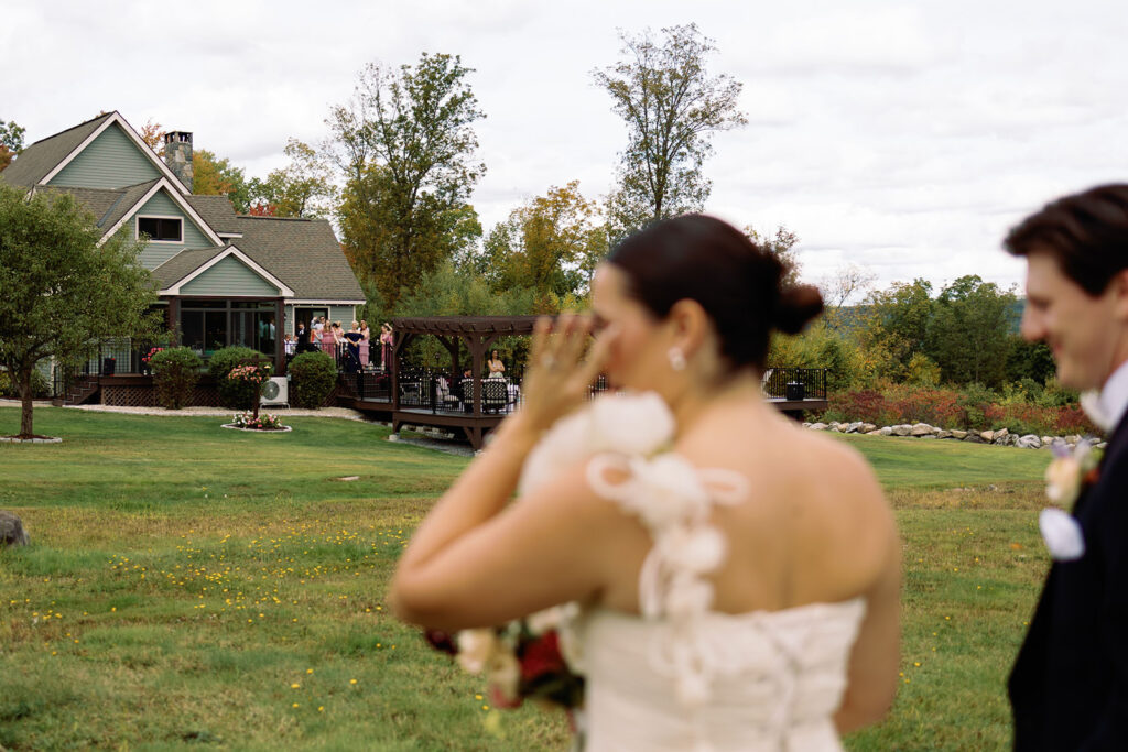 A bride wipes her eye as she tears up and the groom walks beside her outdoors.