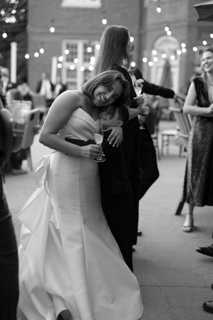 A bride hugging a child and smiling while holding champagne.