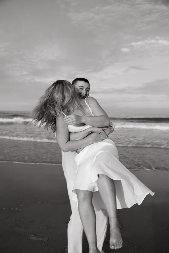 A man picking up a woman and spinning her on the beach during an engagement photo session.