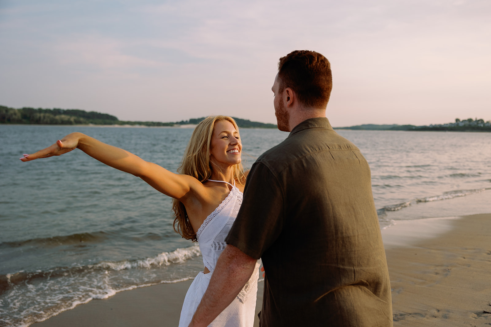 A couple taking engagement photos on the beach and laughing together.