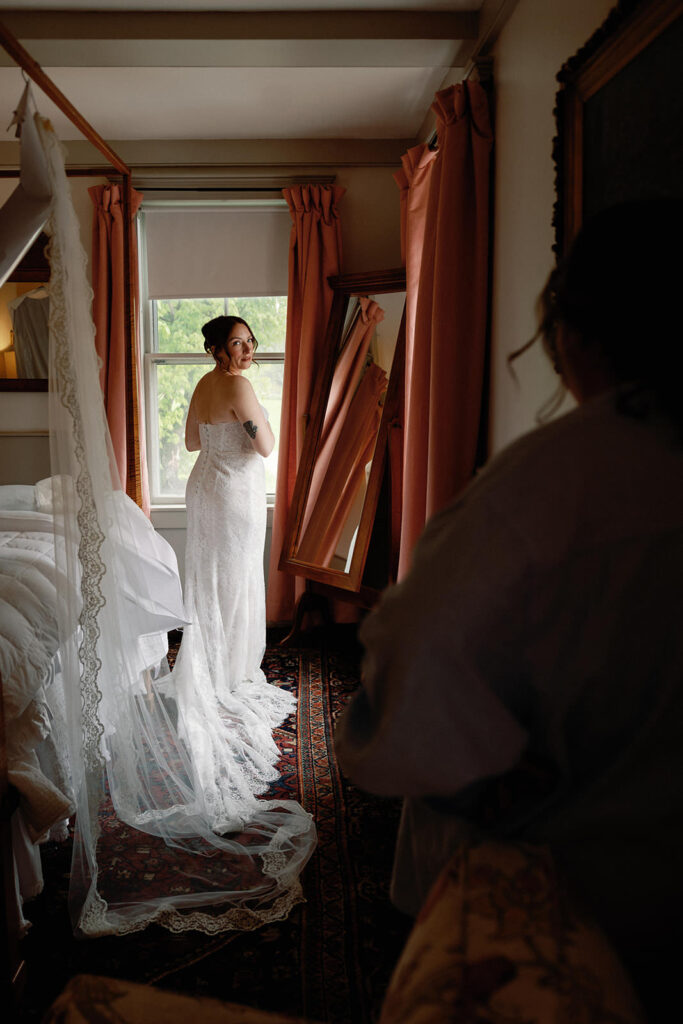 bride puts on wedding dress while looking back at her mom