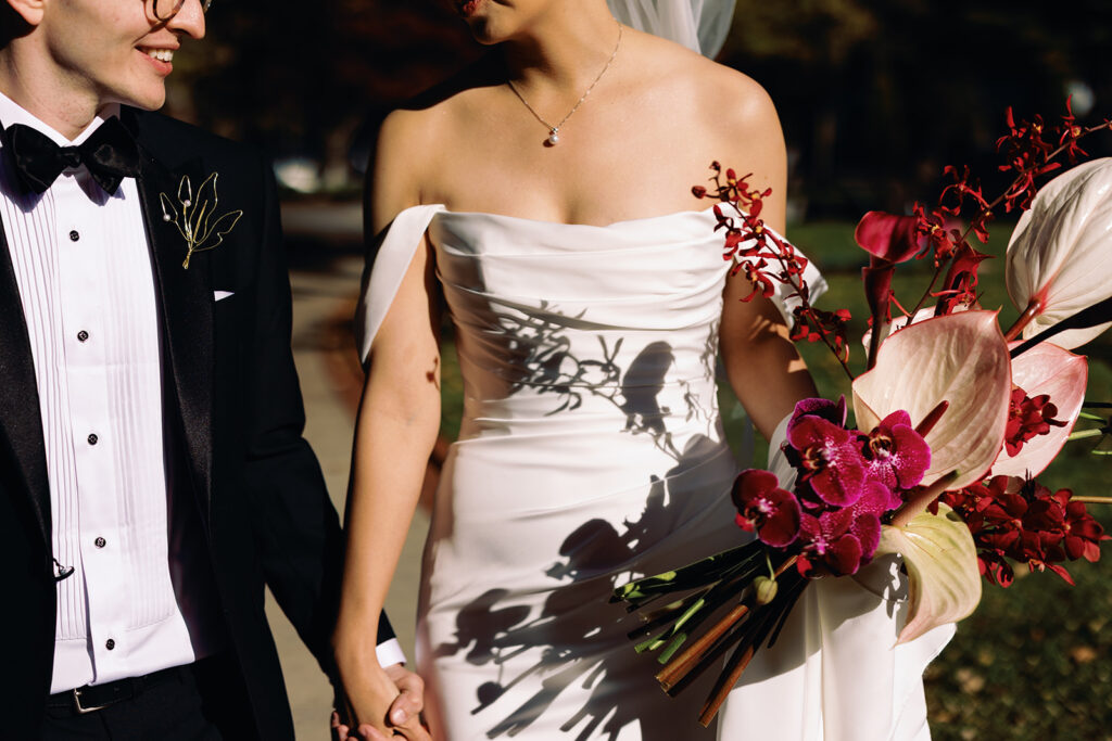 lived in detail shot of bride and groom holding hands in the sunshine with her artistic and sculptural wedding bouquet designed by Rococo Floral